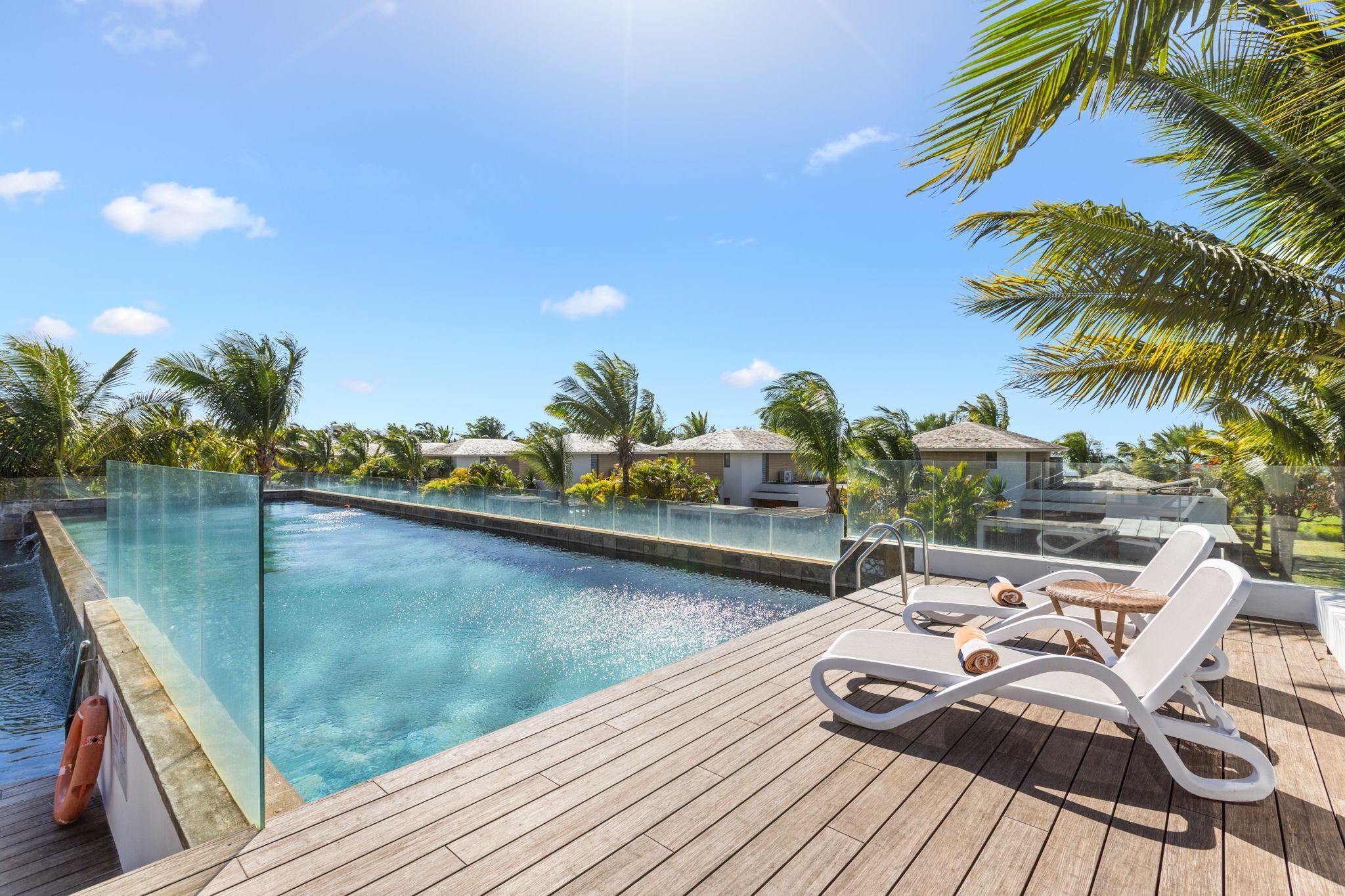 A clear pool with lounge chairs, a wooden deck, and palm trees.