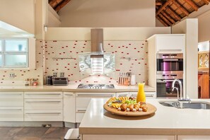 A modern kitchen with a central island, a built-in oven, and a stainless steel range hood. - Villa Bezweni (Cape Town)