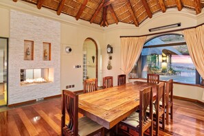 A dining area with a large wooden table and chairs, a fireplace, and a view of the outdoors. - Villa Bezweni (Cape Town)