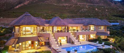 A modern house with a pool, surrounded by lush greenery and mountains in the background.