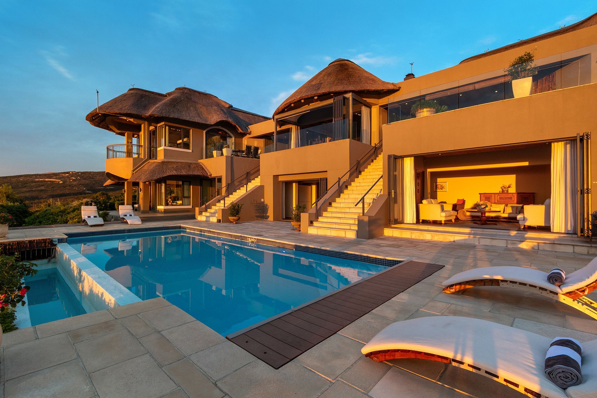 Una villa moderna con piscina, mobiliario exterior y una escalera que lleva a un segundo piso.