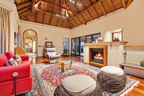 Ein geräumiges Wohnzimmer mit hoher Holzbalkendecke, Kamin, rotem Sofa und großem gemusterten Teppich.