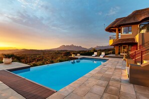 A swimming pool with a view of mountains, a wooden deck, and a modern house with a balcony. - Villa Bezweni (Cape Town)