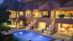 Une maison à plusieurs étages avec une piscine, un espace salon extérieur et une vue sur les montagnes.
