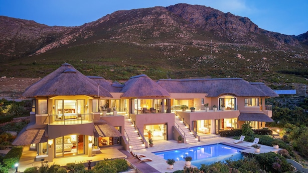 Une maison moderne avec une piscine, entourée d’une végétation luxuriante et avec des montagnes en toile de fond.