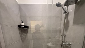 A modern shower stall with a glass door, a handheld showerhead, and a wall-mounted faucet. - Cozy 1BR Apt Walk to Westbahnhof (Vienna)