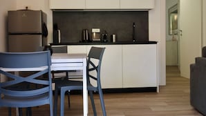 Ett kompakt kök med kylskåp, kaffebryggare och diskho. I vardagsrummet finns ett matbord med stolar och en soffa.