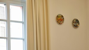 Ett rum med ett matbord, två stolar, ett fönster med gardiner och två väggdekorationer.