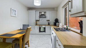 Una cocina compacta con armarios blancos, una mesa de comedor de madera y una lámpara colgante.