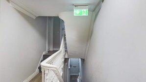 Una escalera con barandilla blanca, un letrero de salida de emergencia verde y una puerta al final.