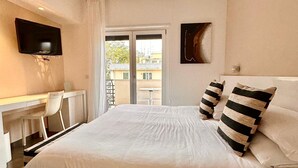 Een slaapkamer met een groot bed, een bureau, een stoel, een aan de muur bevestigde televisie en een raam met gordijnen.