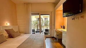 Een hotelkamer met een groot bed, een bureau, een flatscreen televisie en een balkon met buitenmeubels.