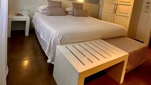 Een slaapkamer met een bed, nachtkastjes, een bankje en een kledingkast.