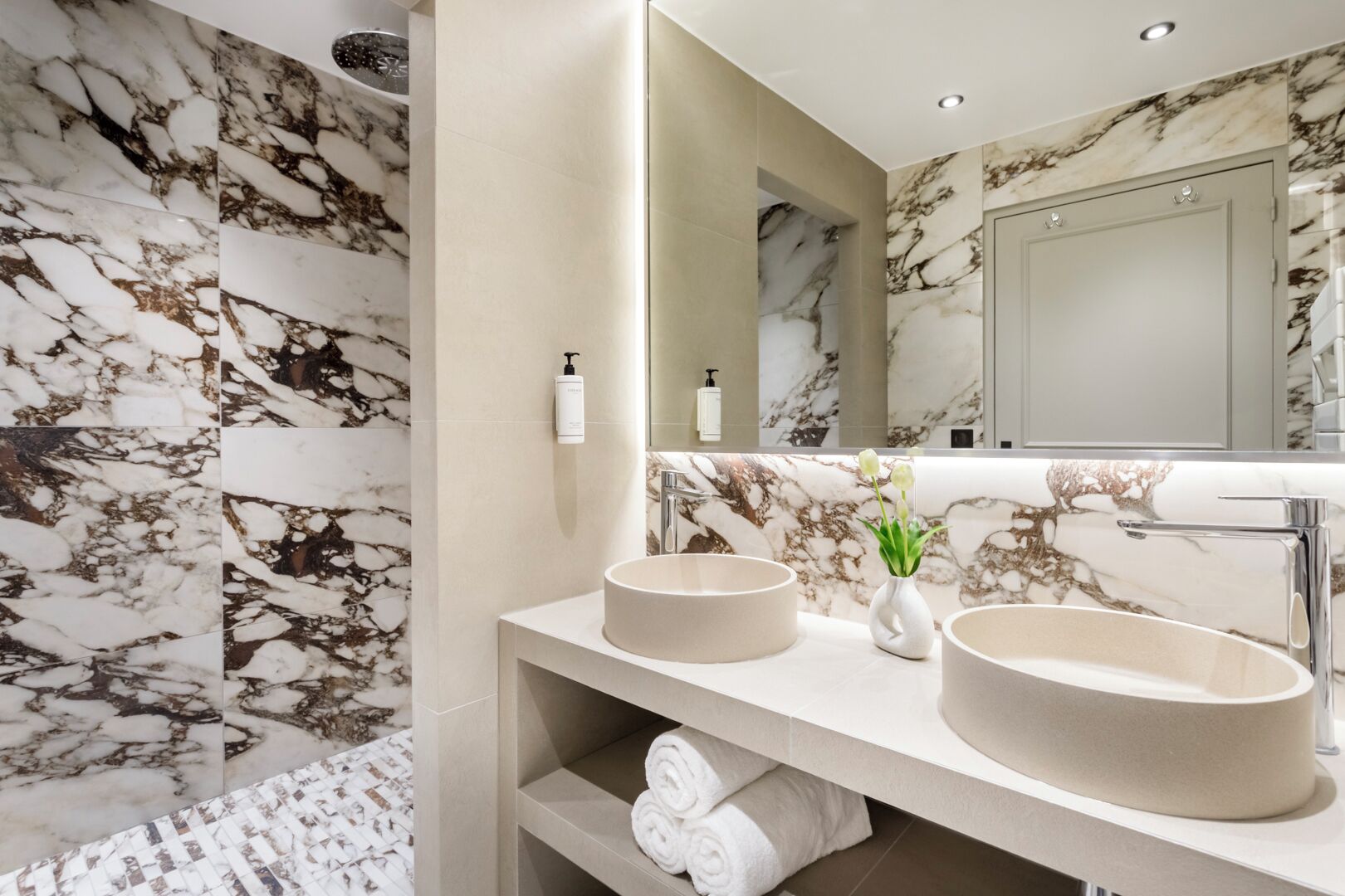 A bathroom with marble walls, two sinks, a mirror, and a towel rack.