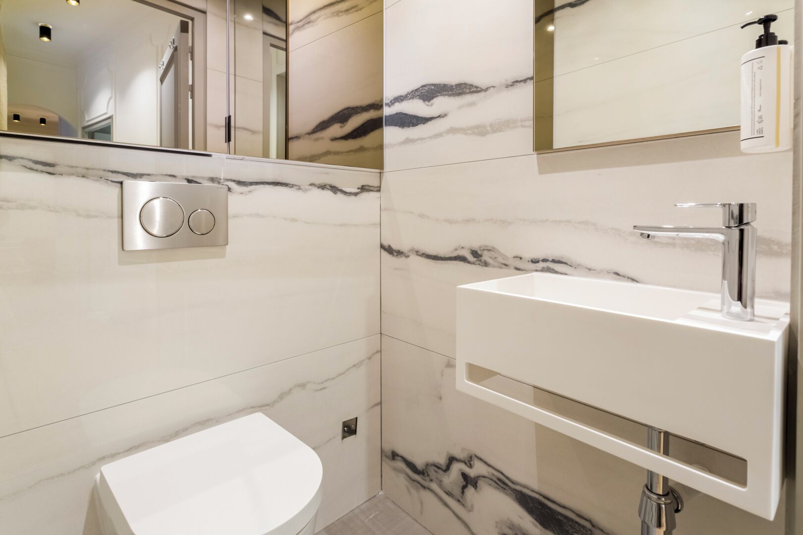 A modern bathroom with a marble wall, a white sink, and a mirror.