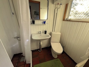 Ein Badezimmer mit weißem Waschbecken, WC und Dusche. Ein Fenster mit weißem Rahmen und eine grüne Matte liegen auf dem Boden.