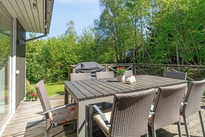 A wooden deck with a table and chairs, a grill, and potted plants.