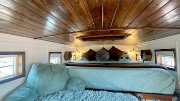 Een slaapkamer met een houten plafond, een bed met een blauwe deken en twee ramen.