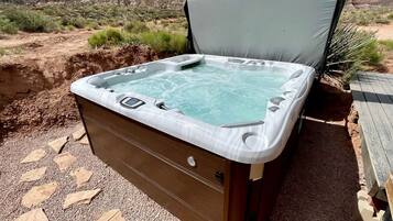 A hot tub with a wooden exterior, set in a desert landscape with rocky hills in the background.