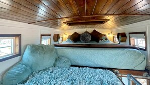 Une chambre avec un plafond en bois, un lit recouvert d’une couverture bleue et deux fenêtres.