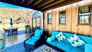 Un espacio de estar al aire libre techado, con piso de madera, un sofá de mimbre y una mesa con una planta en maceta.