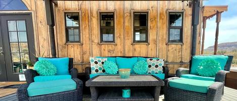 A wooden deck with wicker furniture, a table, and a view of a mountainous landscape.
