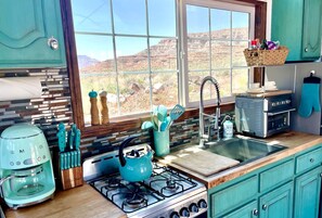 A kitchen with a gas stove, a coffee maker, a toaster, and a window with a view of a desert landscape.