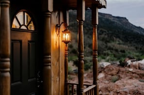 Ein Holzhaus mit einer dunklen Tür, einem Fenster mit Rundbogen und einem Laternen an der Veranda.