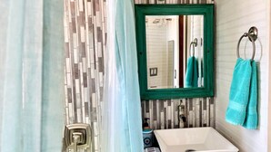 Un baño con salpicadero de azulejos, un lavabo blanco, un espejo con marco verde y un perchero con toalla.