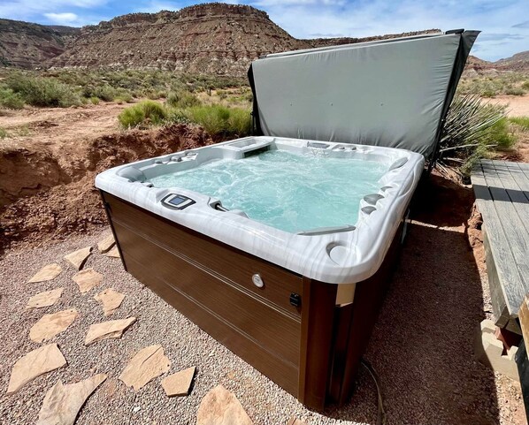 A hot tub with a wooden exterior, set in a desert landscape with rocky hills in the background.