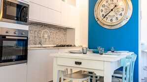 Una cocina moderna con armarios blancos, una pared de acento azul, un reloj grande y una zona de comedor con sillas blancas y azules.