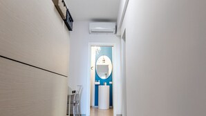 Un pasillo estrecho con una pared blanca y una puerta al final que da a un baño.