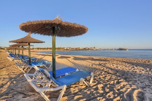 A beach with rows of sun loungers and thatched umbrellas.