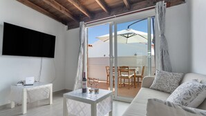 A living room with a sofa, a coffee table, a TV, and a sliding glass door leading to an outdoor area with a table and chairs. - Holiday Home 'Casa Vista Golf' with Sea View, Shared Pool & Wi-Fi (Castillo Caleta de Fuste)