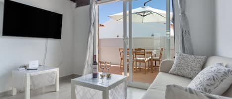 A living room with a sofa, a coffee table, a TV, and a sliding glass door leading to an outdoor area with a table and chairs.