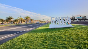 A road sign with 'SAHARA' and 'FUEGUEVENTURA' text, surrounded by grass and palm trees. - Holiday Home 'Casa Vista Golf' with Sea View, Shared Pool & Wi-Fi (Castillo Caleta de Fuste)