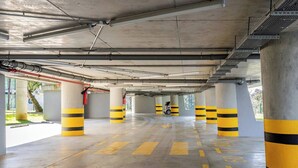 An underground parking garage with concrete pillars, yellow and black striped bollards, and directional arrows on the floor. - Elite condo, Sea View at Batumi Botanical Gardens interior by 3-Kopheli (Batumi)