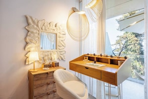 Una habitación moderna con un escritorio de madera, una silla blanca, un adorno en la pared y un amplio ventanal con vistas.