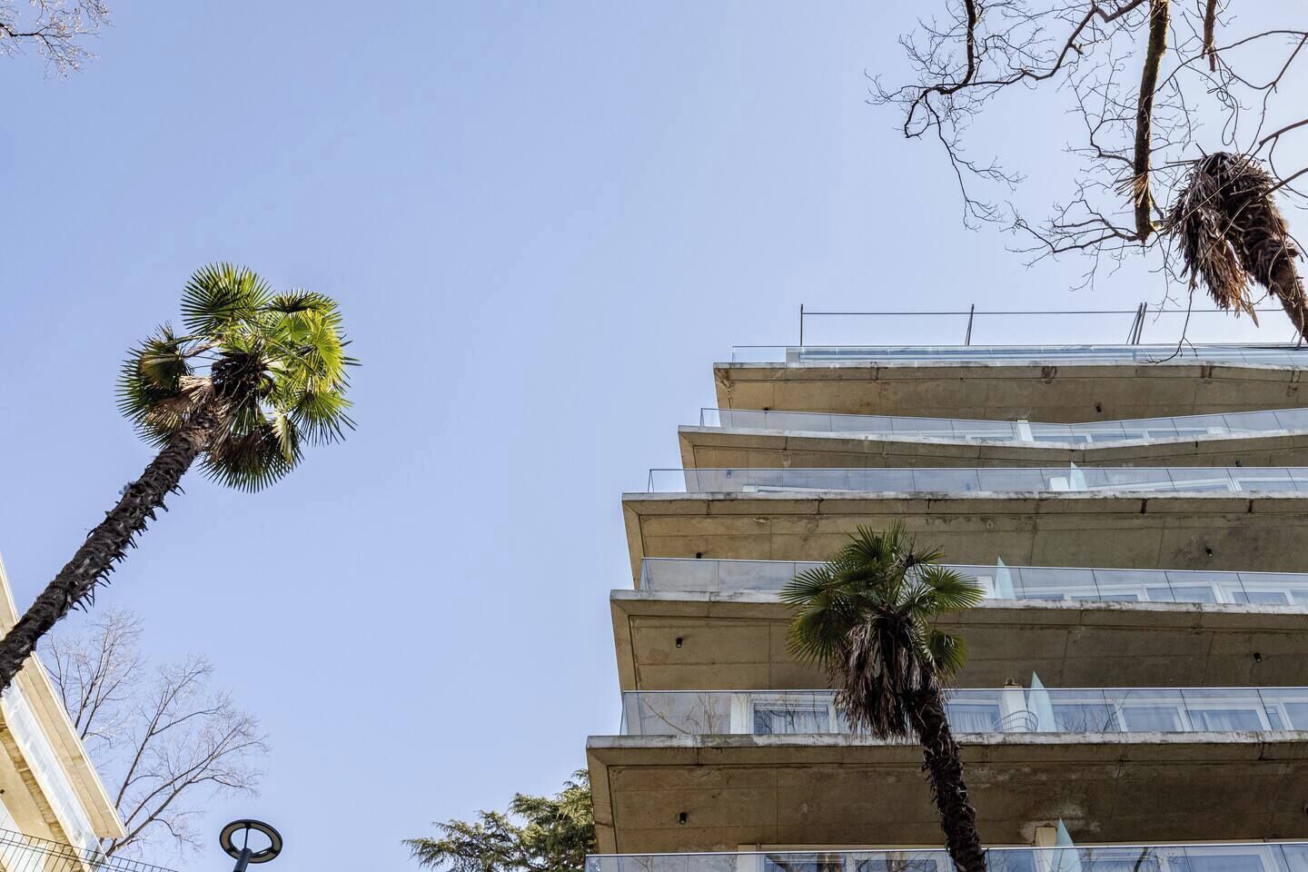 Um edifício de vários andares com varandas e palmeiras.