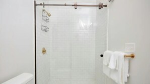 A modern bathroom with a glass-enclosed shower, white tiled walls, a white sink, and a towel rack.