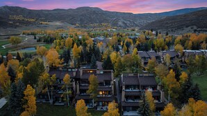 A residential area with modern multi-story buildings, surrounded by autumn-colored trees and a mountainous backdrop.