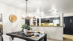 A modern kitchen with dark cabinets, a black countertop, and a dining area with a dark table and white chairs.