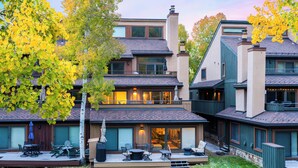 A modern two-story house with a patio area, large windows, and a chimney.