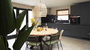 A modern kitchen with dark cabinets, a round wooden table, and two green chairs. - Fokkemaat - Modern family home with large garden, close to the beach and town center (Callantsoog)