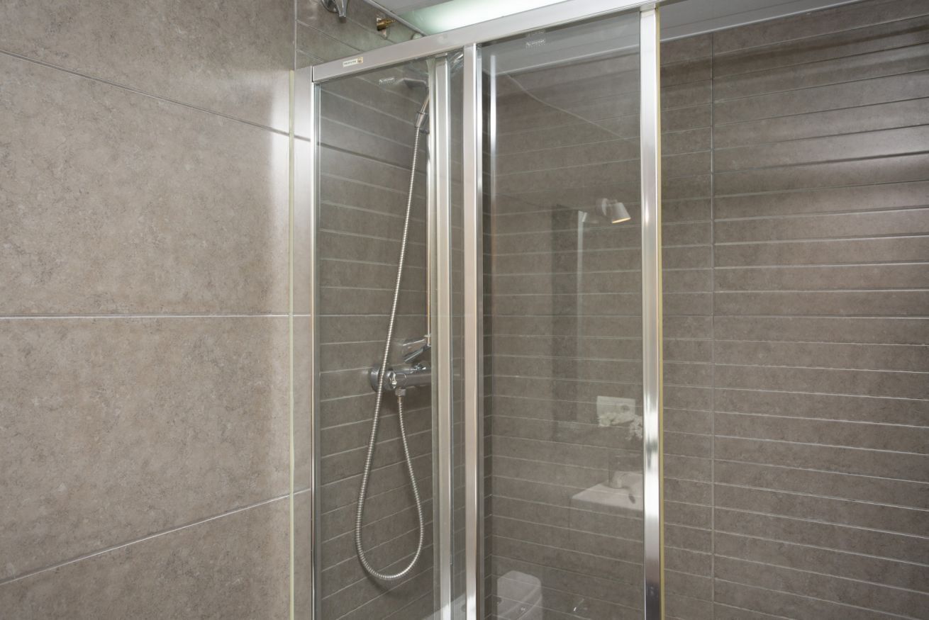 Une douche avec une porte en verre, des murs carrelés et un pommeau de douche visible.