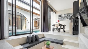 A modern living room with a large window, a pool view, a dining area, and a kitchen. - Luxe Private Pool Villa Santisya 4, 4min-beach by Orivista (Mengwi)