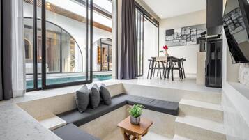 A modern living room with a large window, a pool view, a dining area, and a kitchen.