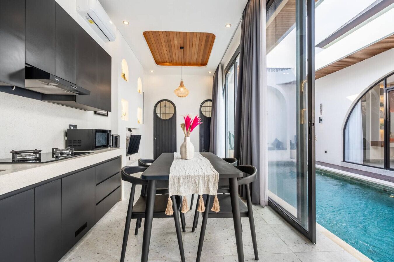 A modern kitchen with dark cabinetry, a wooden ceiling, and a dining area with a table and chairs.