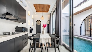 A modern kitchen with dark cabinetry, a wooden ceiling, and a dining area with a table and chairs. - Luxe Private Pool Villa Santisya 4, 4min-beach by Orivista (Mengwi)