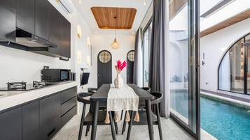 A modern kitchen with dark cabinetry, a wooden ceiling, and a dining area with a table and chairs.